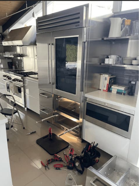 Sub-Zero PRO 48 BI-48SD built-in glass-door refrigerator mid-repair beside a Wolf range in a luxury Miami kitchen — sealed-system service by a certified Sub-Zero technician