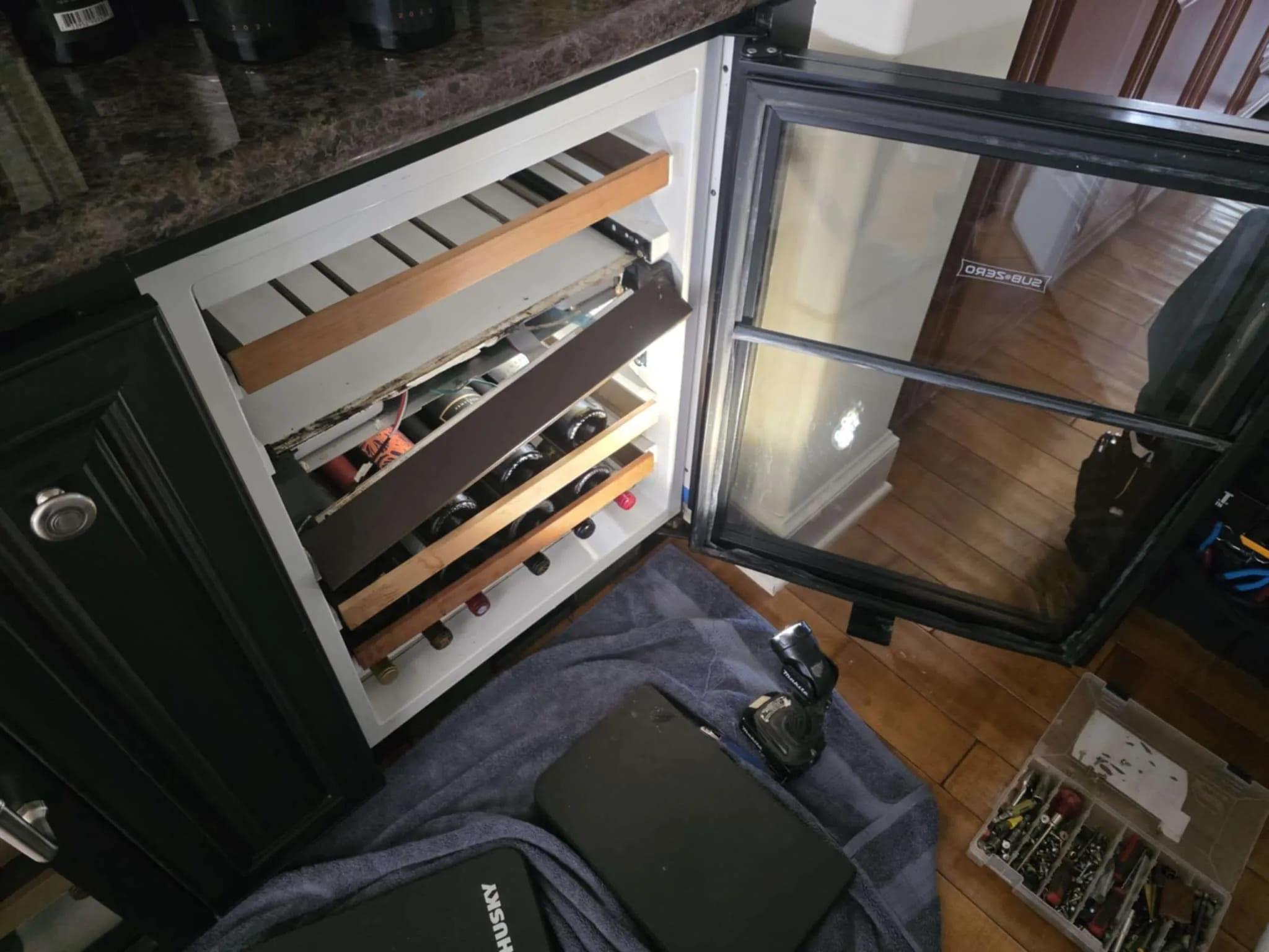 Open Sub-Zero wine cooler with wood racks and bottles being serviced in Miami
